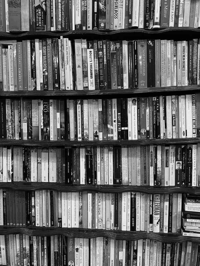 A black and white photo of a bookshelf neatly filled with a variety of books.