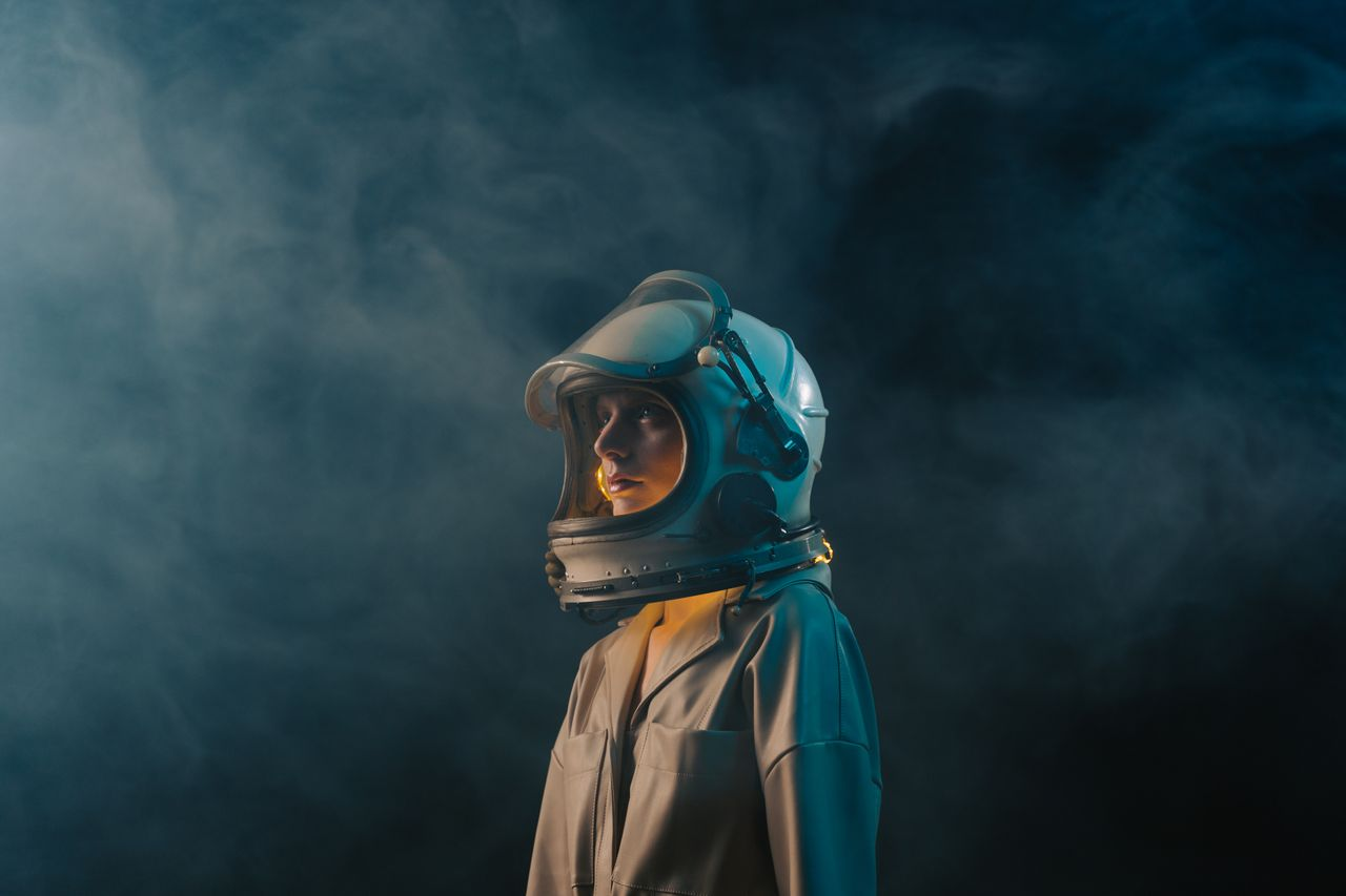 Woman posing in an astronaut costume against a foggy, cosmic backdrop. Moody and imaginative scene.